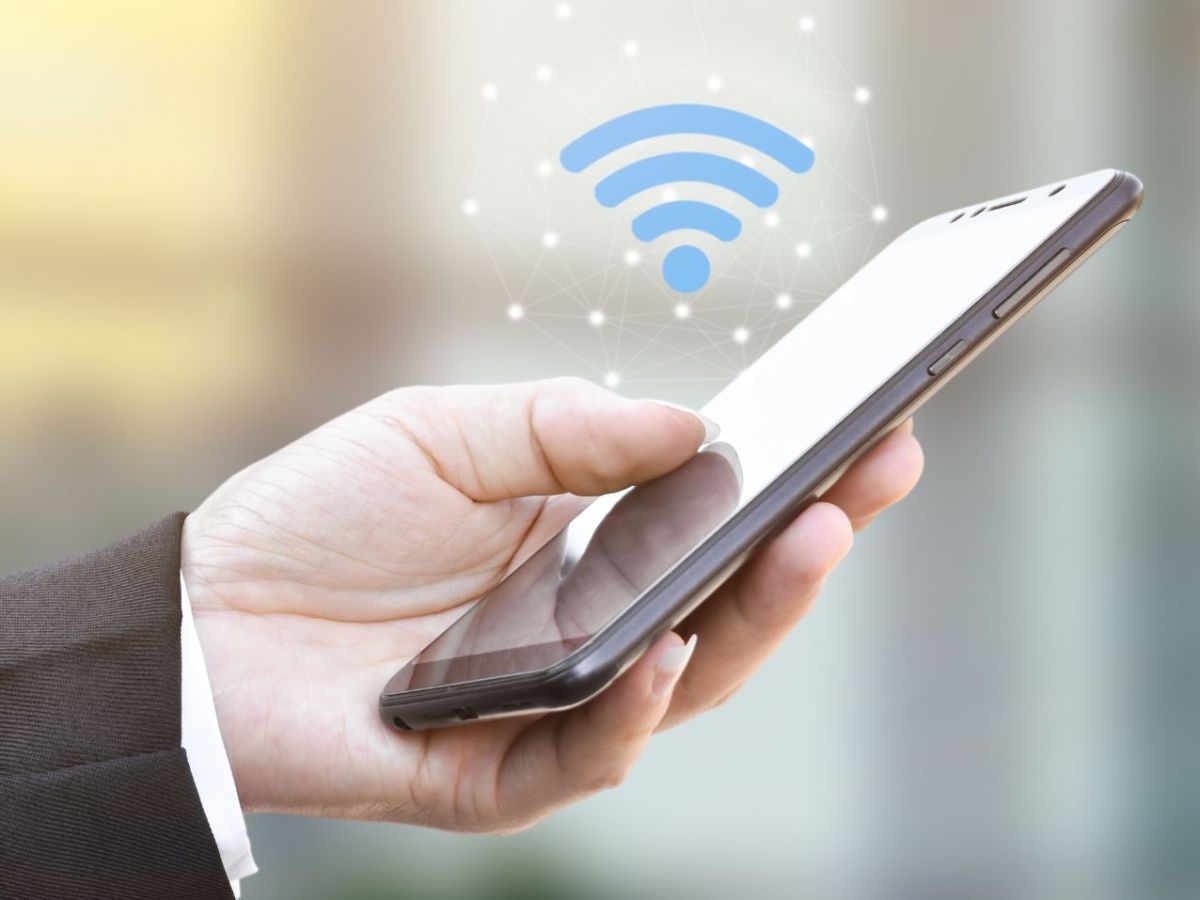 Person hÃ¤lt ein Handy in der Hand, Ã¼ber das ein WLAN-Symbol erscheint.
