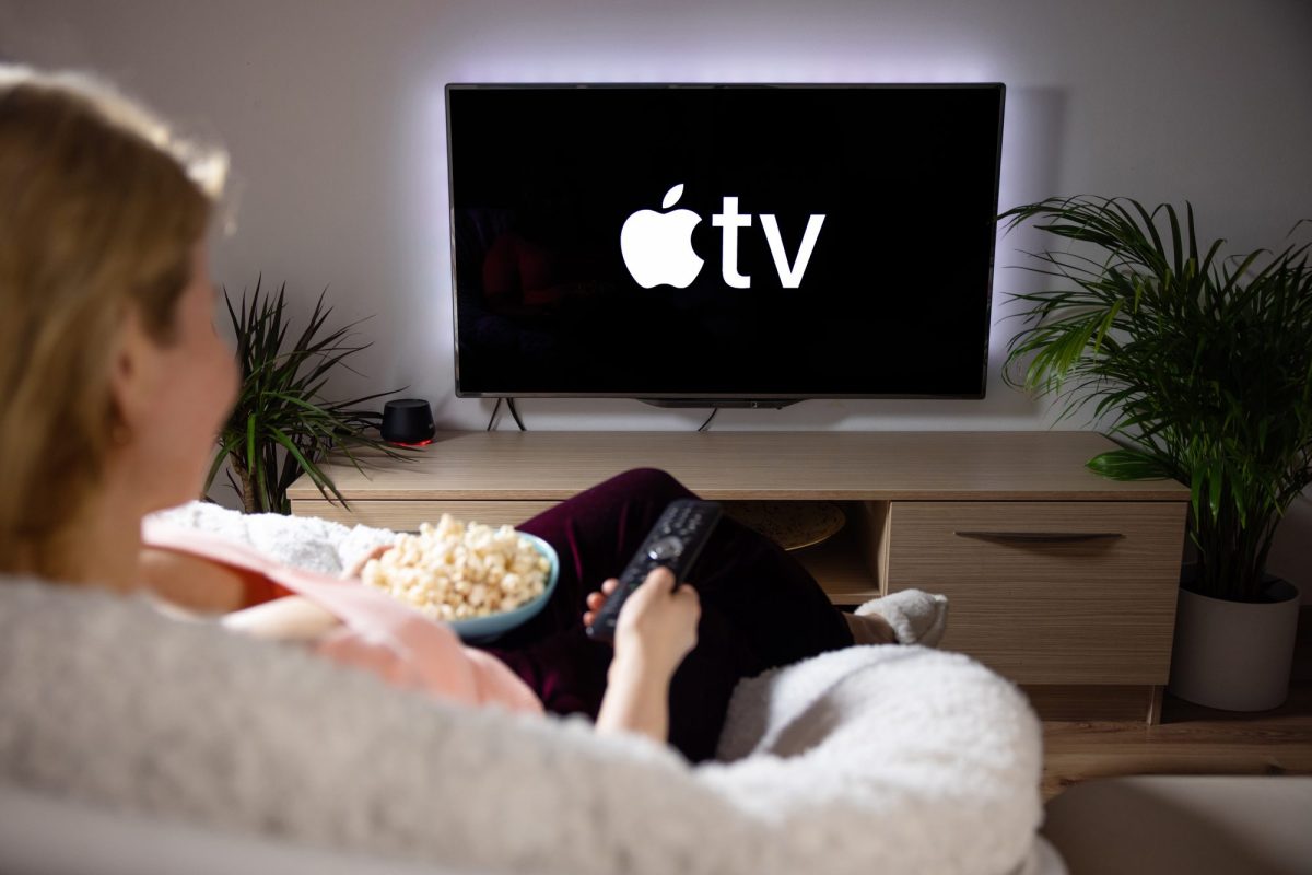 Frau bedient einen Apple TV mit der Fernbedienung vom Sofa aus.