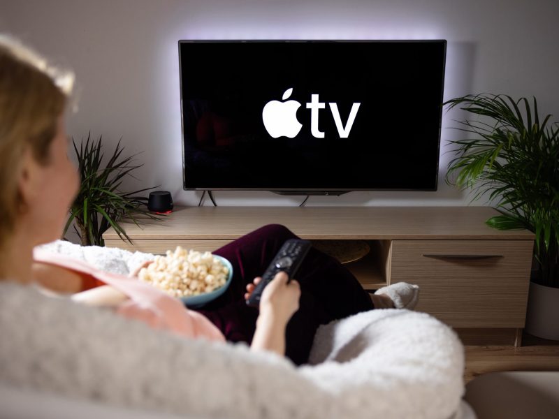 Frau bedient einen Apple TV mit der Fernbedienung vom Sofa aus.
