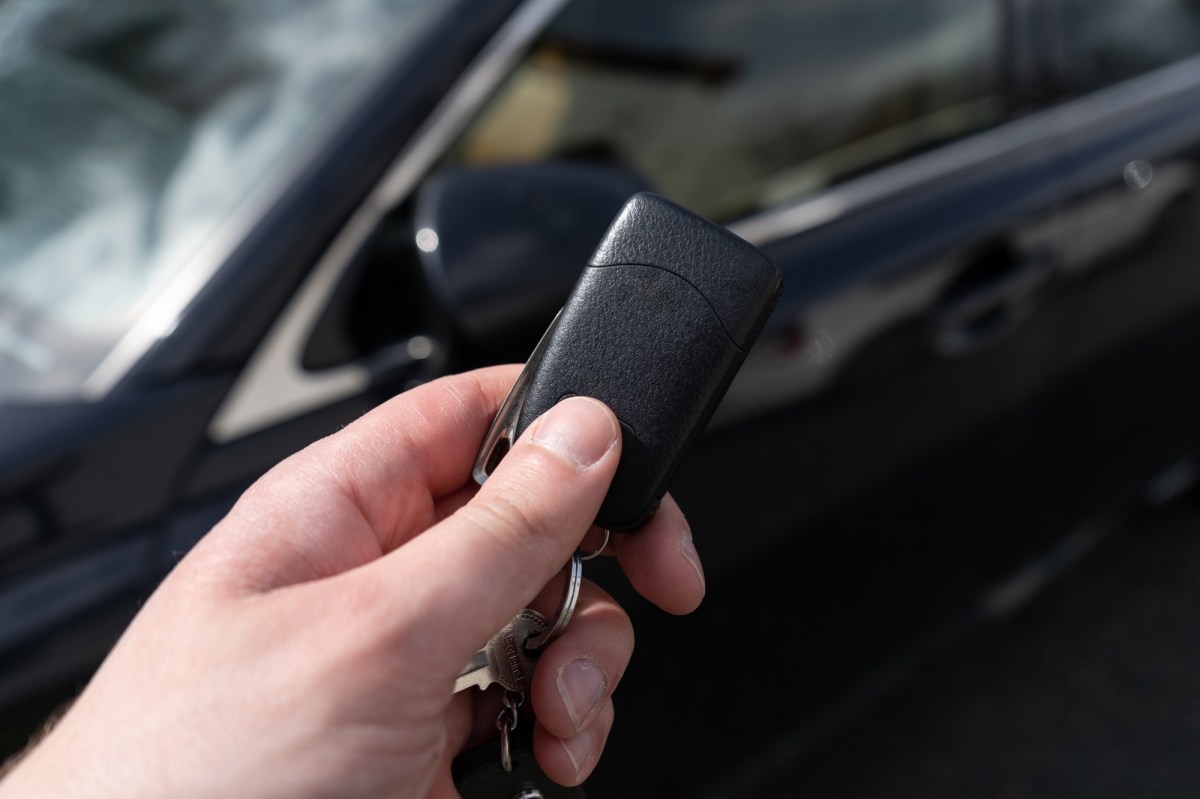 Person hält einen Autoschlüssel vor einem schwarzen Auto hoch