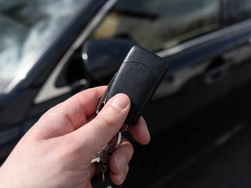 Person hält einen Autoschlüssel vor einem schwarzen Auto hoch