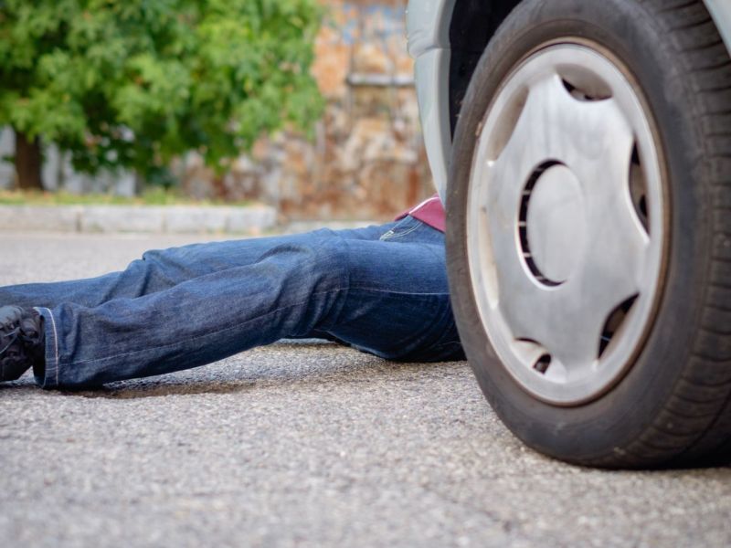 Person liegt tot vor oder hinter einem Auto.