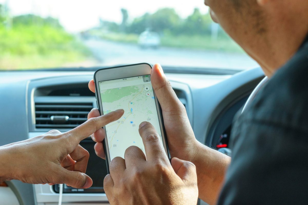 Zwei Personen in Auto deuten auf Smartphone-Bildschirm, der Google Maps anzeigt.