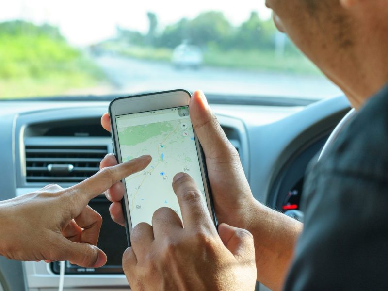 Zwei Personen in Auto deuten auf Smartphone-Bildschirm, der Google Maps anzeigt.