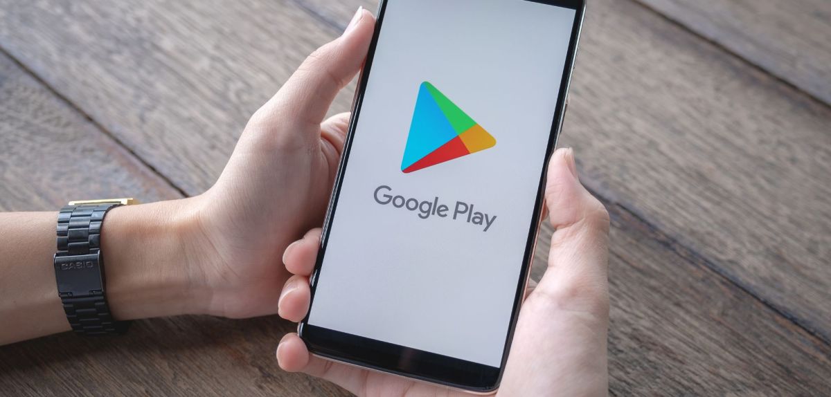 Person hält Handy mit dem Google Play Store auf dem Display in Händen.