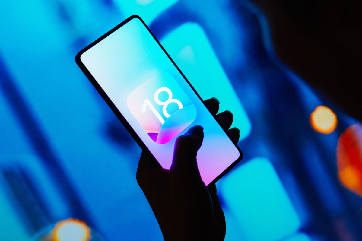 Smartphone in einer Hand zeigt das iOS 18-Logo.