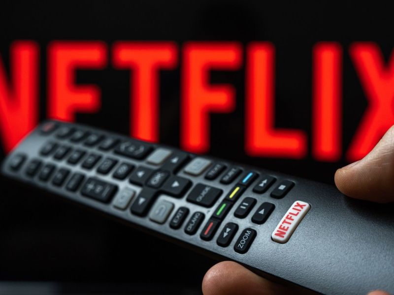 Person hält Fernbedienung vor ein Fernseher mit Netflix.