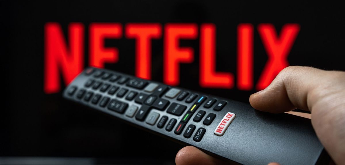 Person hält Fernbedienung vor ein Fernseher mit Netflix.