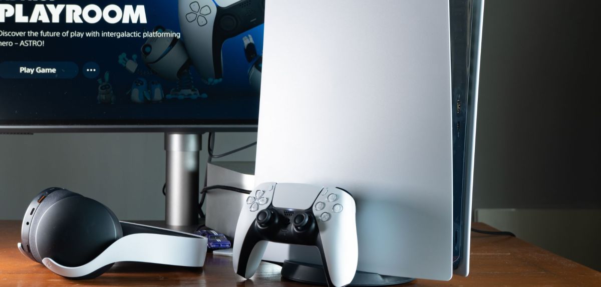 Eine PlayStation 5 mitsamt Controller und Headset vor einem Monitor.