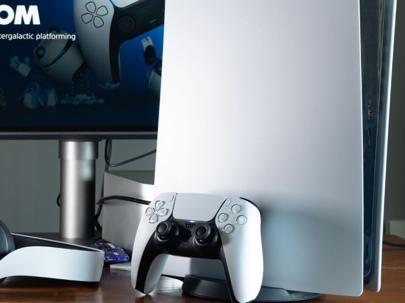 Eine PlayStation 5 mitsamt Controller und Headset vor einem Monitor.