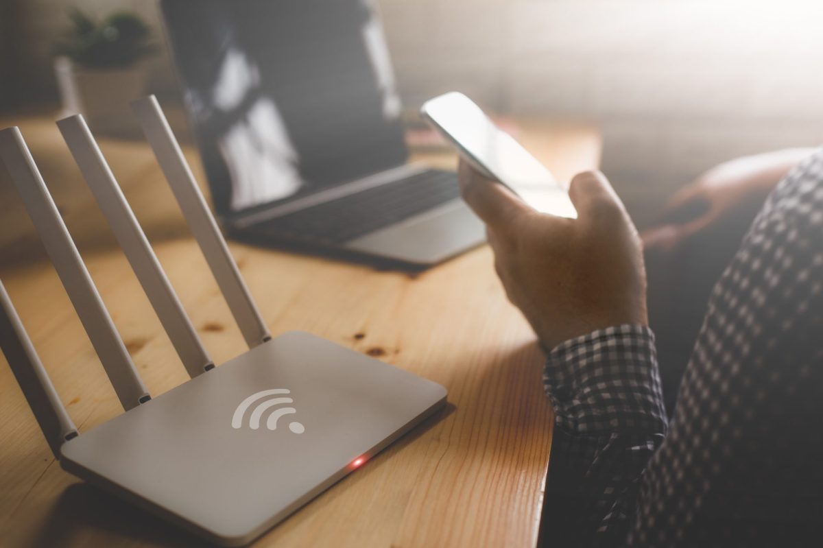 Person sitzt mit Handy vor dem WLAN-Router