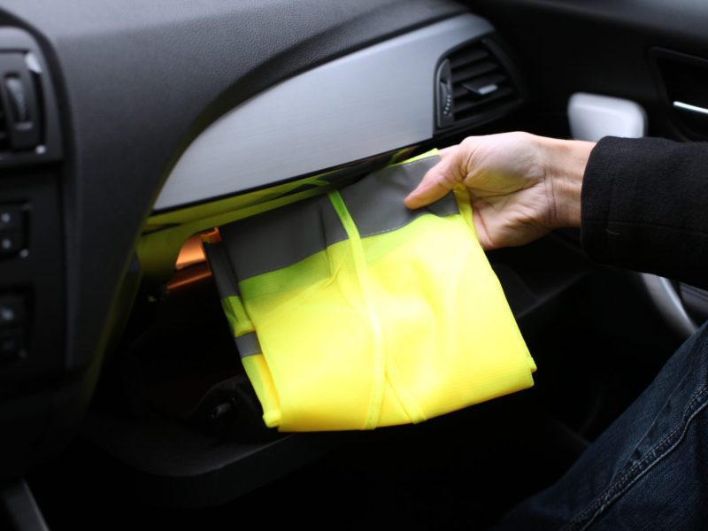 Person zieht eine Warnweste aus dem Handschuhfach ihres Autos.