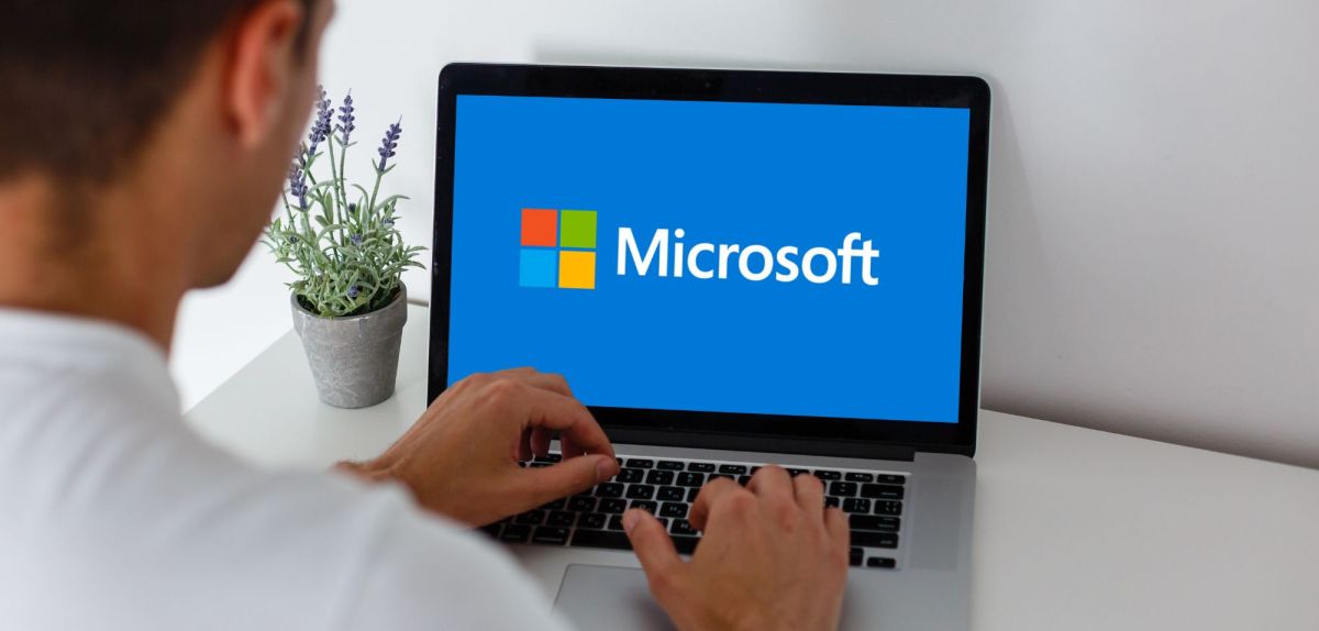 Mann sitzt vor einem Laptop mit einem Microsoft-Logo auf dem Bildschirm.