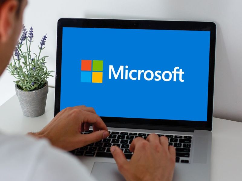 Mann sitzt vor einem Laptop mit einem Microsoft-Logo auf dem Bildschirm.