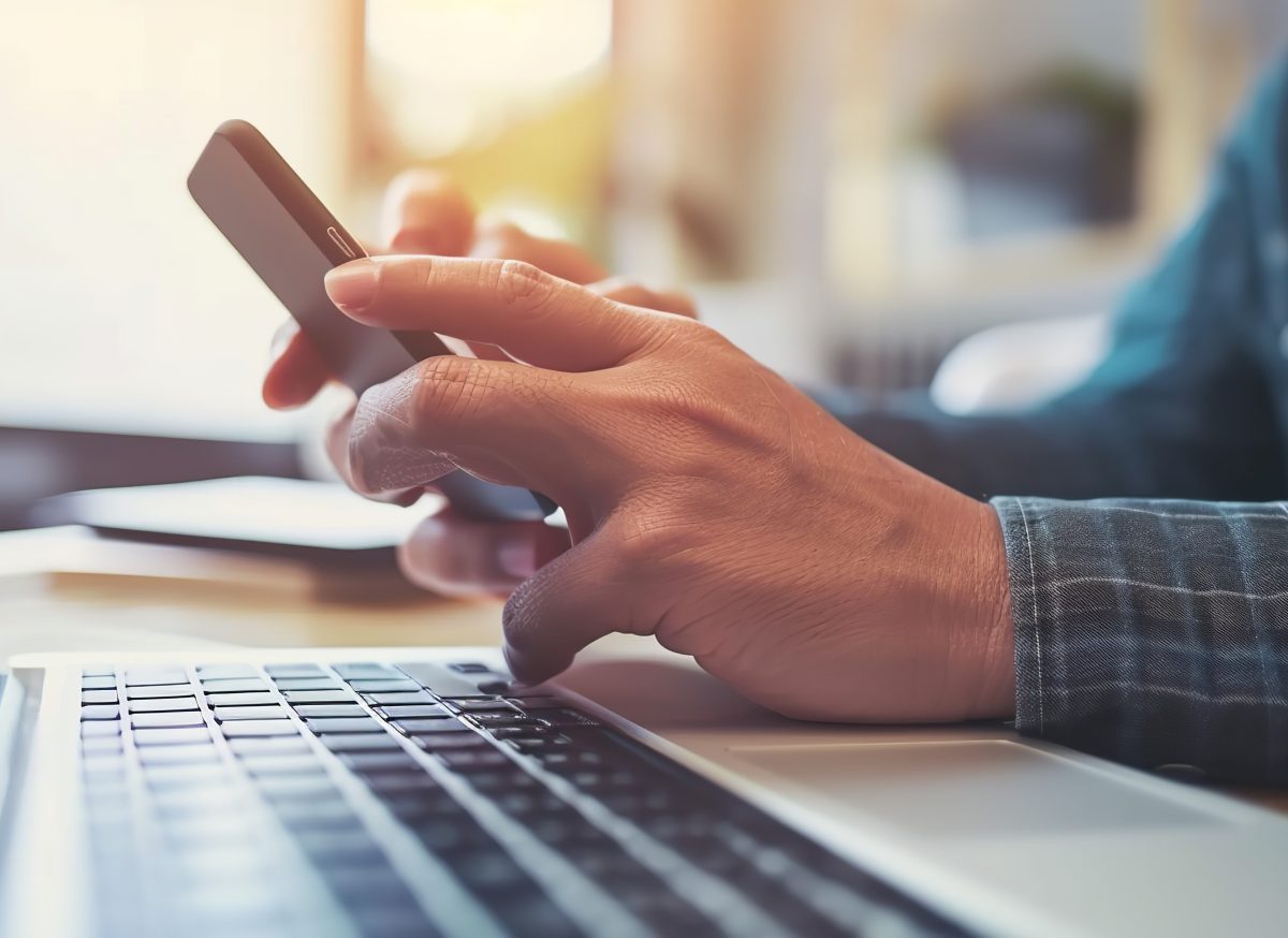 Person mit Smartphone vor einem Laptop