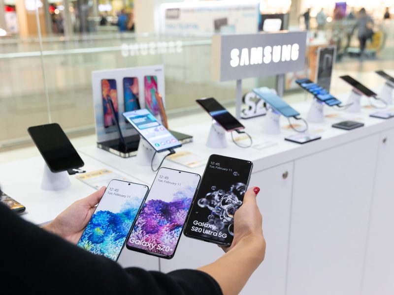 Person hält mehrere Samsung-Handys nebeneinander in einem Laden.