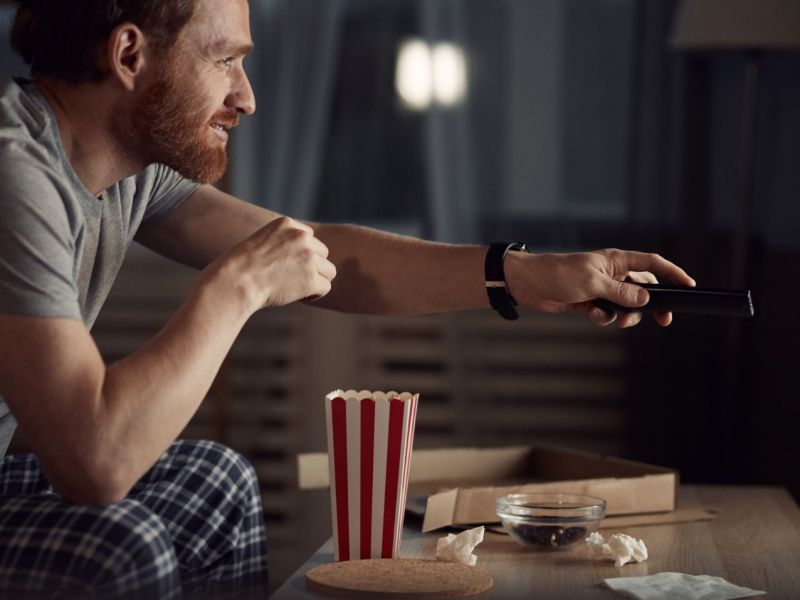 Mann sitzt abends mit Snacks vor dem Fernseher.