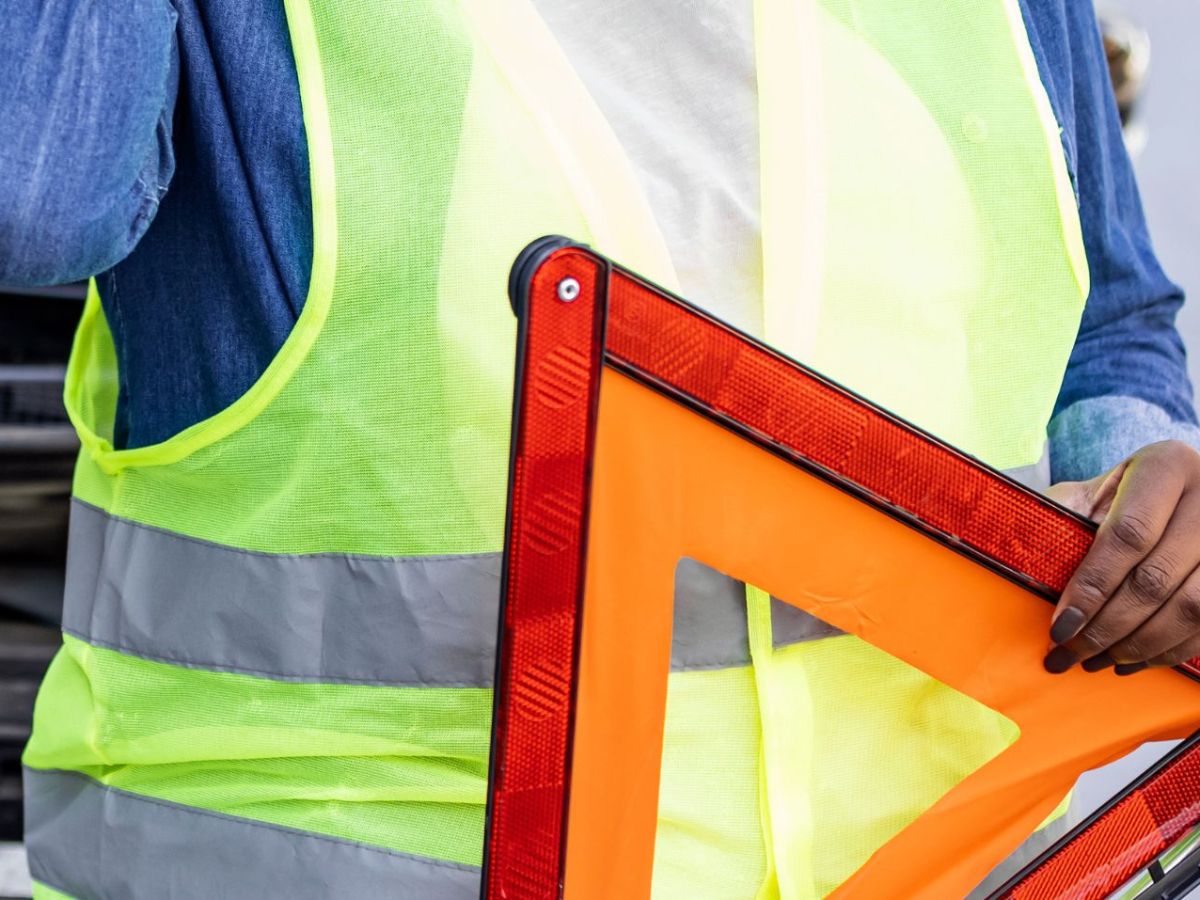 Person mit Warnweste hält ein Warnschild in der Hand.