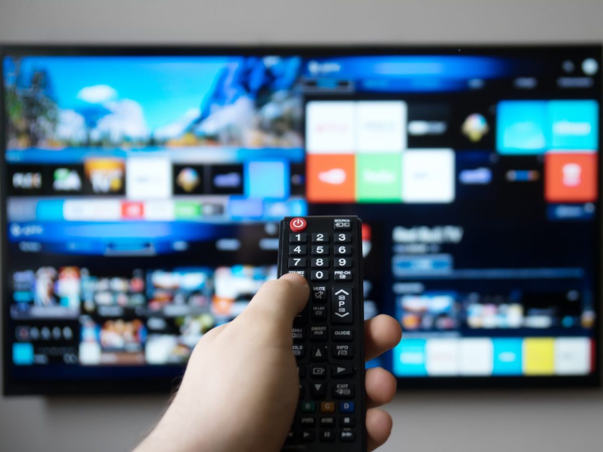 Hand bedient Fernbedienung, die auf einen Smart TV gerichtet ist.