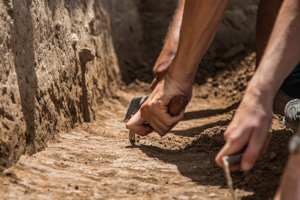 Hände graben mit Werkzeugen an archäologischem Fund.