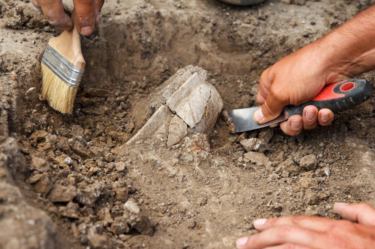 Hände graben mit Werkzeugen an archäologischem Fund.