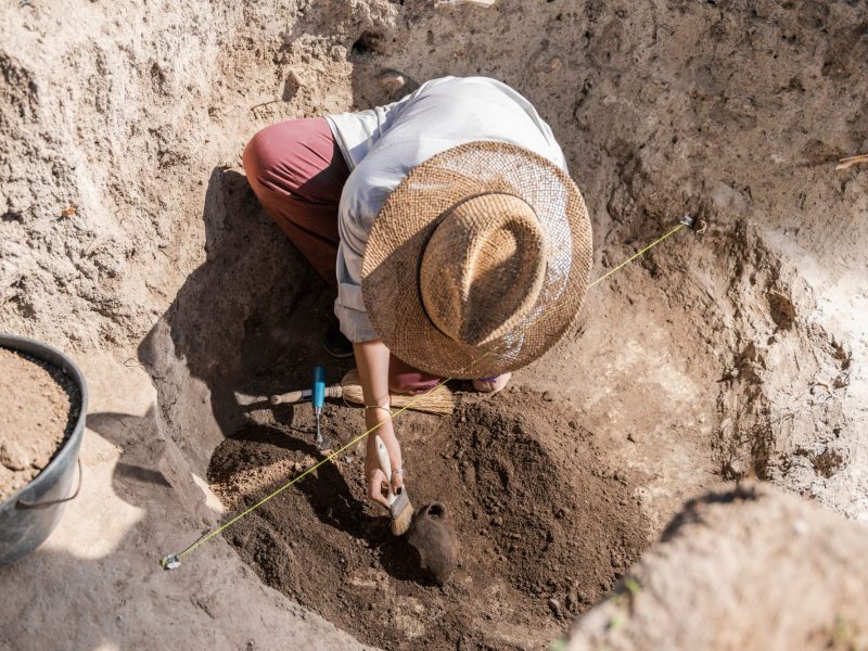 Frau gräbt mit Werkzeug an einem archäologischen Fund.