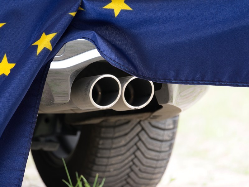 Auto-Auspuff hinter einer EU-Flagge