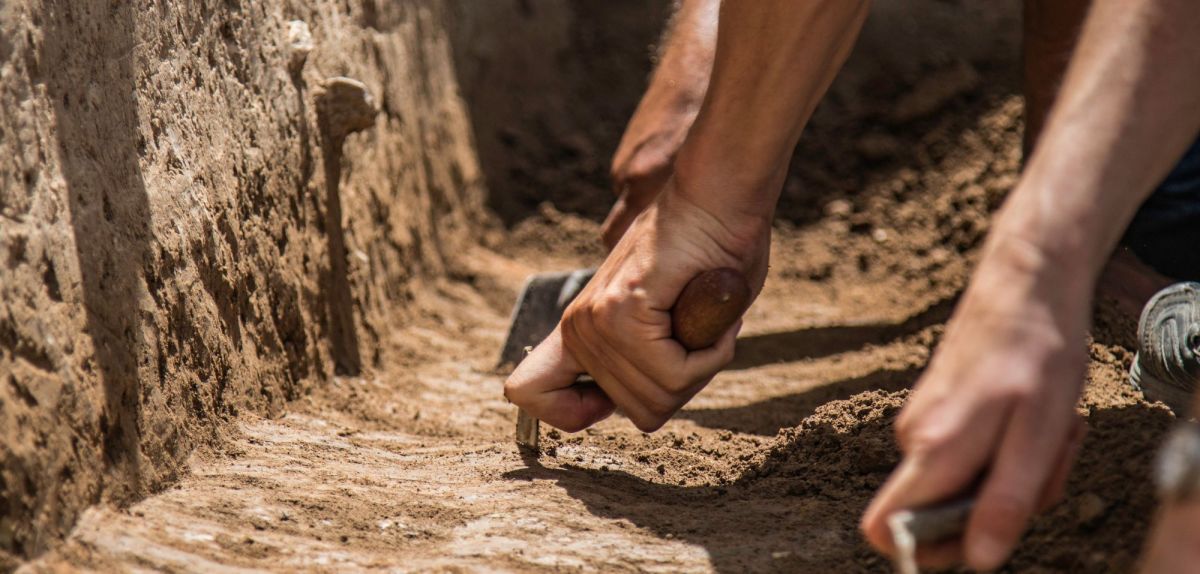 Hände graben mit Werkzeugen an einem archäologischen Fund.