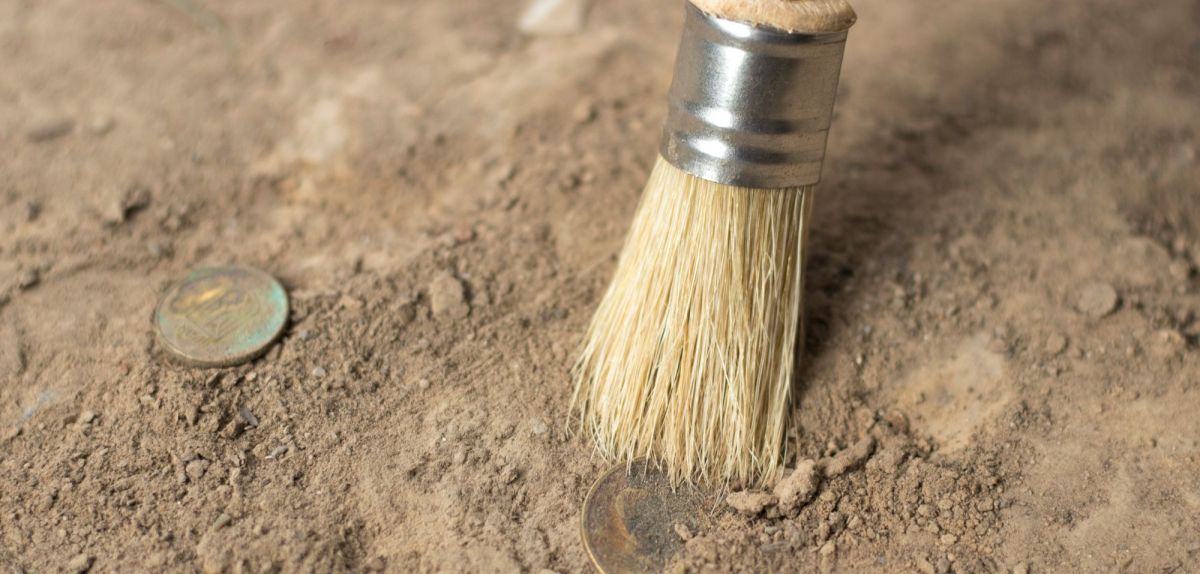 archäologisches Werkzeug arbeitet an einigen Münzen im Sand.