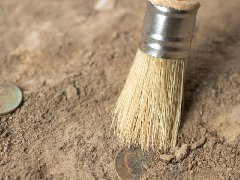 archäologisches Werkzeug arbeitet an einigen Münzen im Sand.