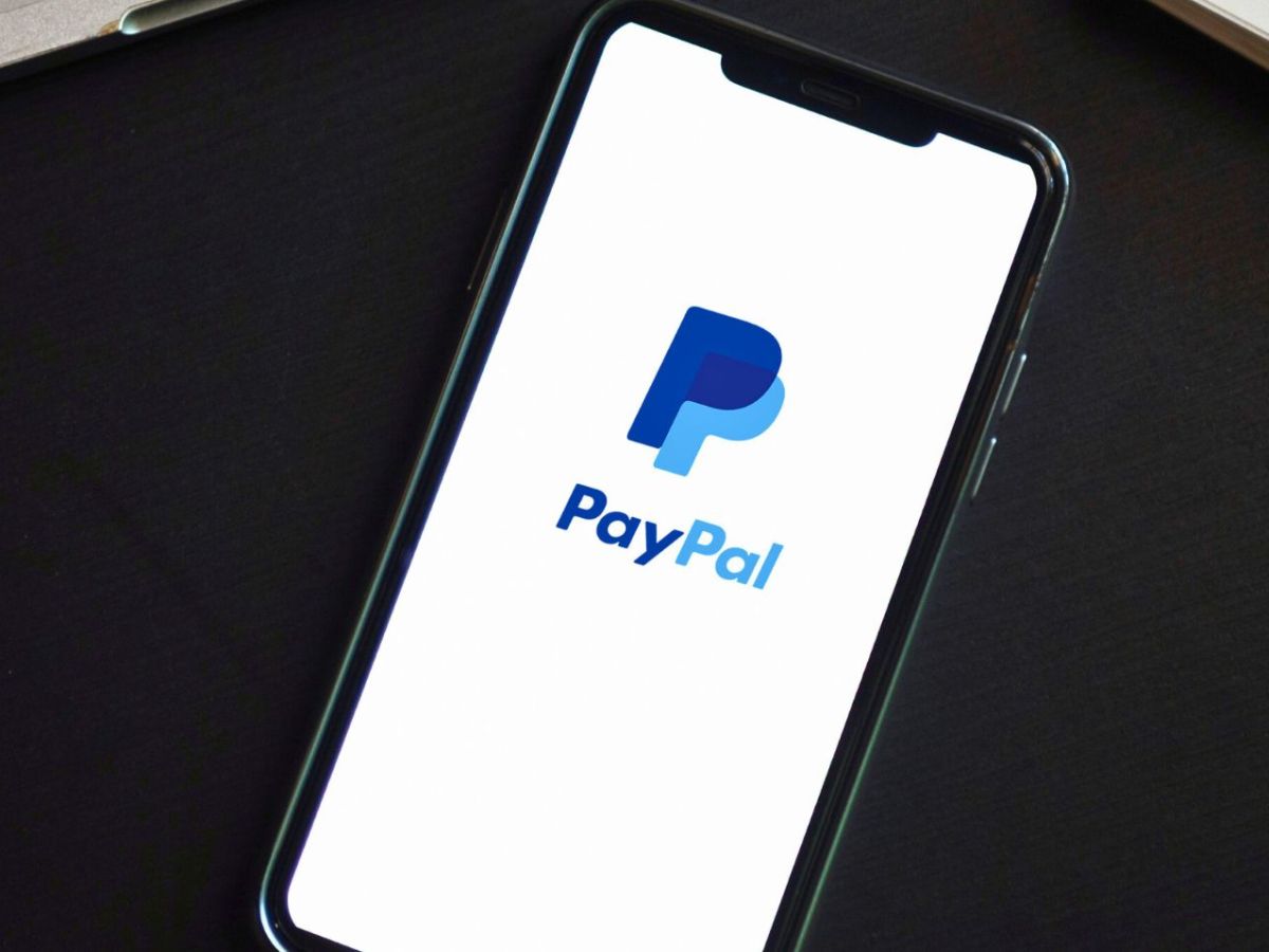 Smartphone mit PayPal-Logo zwischen Laptop und Notizbuch.