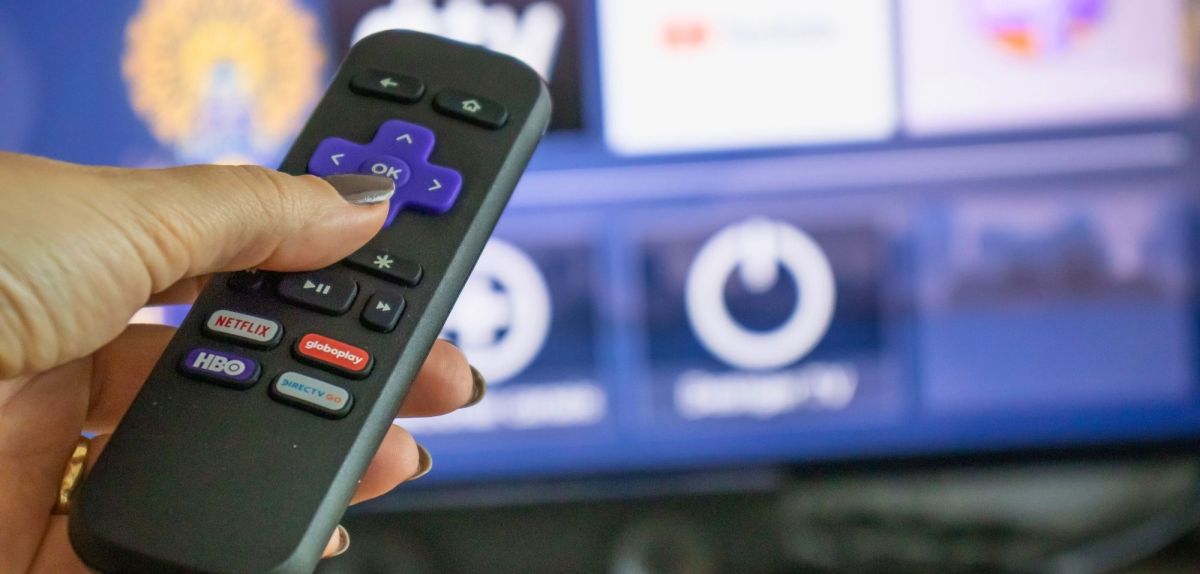 Roku-Fernbedienung mit Streaming-Bildschirm im Hintergrund.