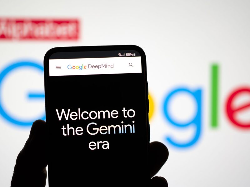 Auf einem Handy-Display steht: Welcome to the Gemini era. Im Hintergrund ist das Google Logo zu sehen.