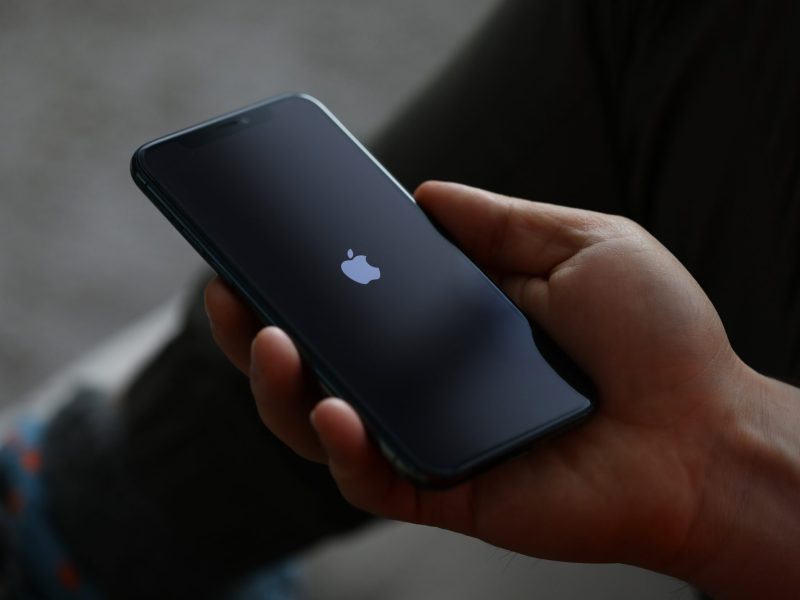Person hält Handy. Auf dem Display wird das Apple-Logo angezeigt.