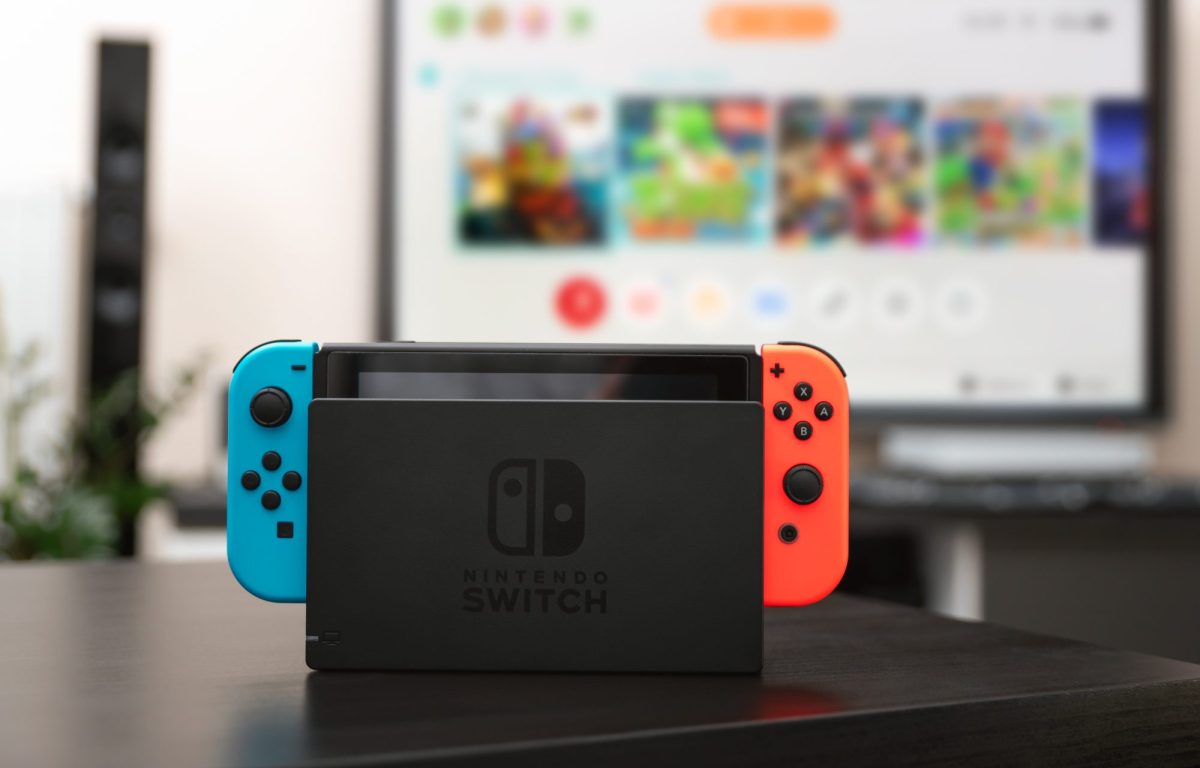 Eine Nintendo Switch-Konsole steht auf einem Tisch vor einem angeschalteten Fernseher.