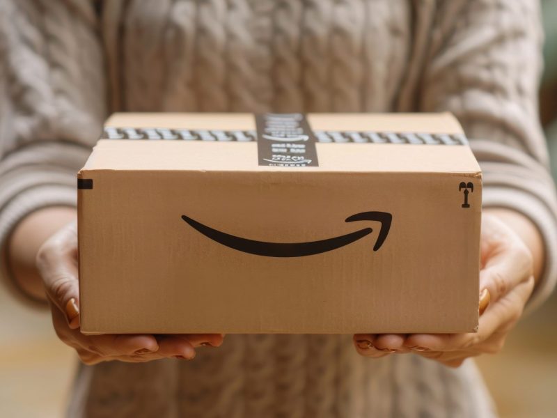 Eine Person hält einen Karton, auf dem das Amazon-Logo abgebildet ist.