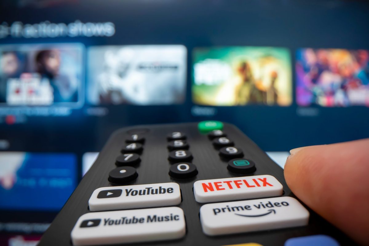 Person hält eine Fernbedienung auf einem Fernseher, auf dem verschiedene Streaming-Angebot angezeigt werden.