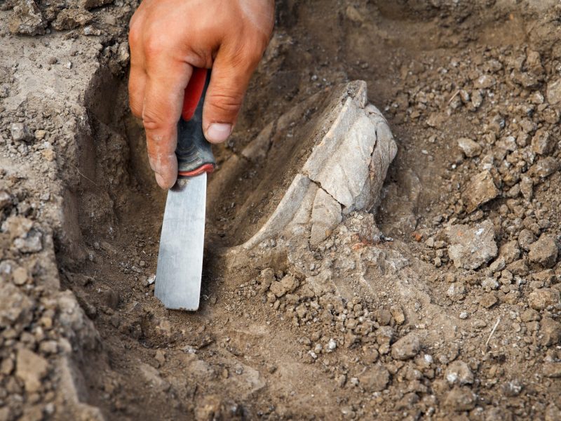Person arbeitet mit Spaten an einem archäologischen Fund.