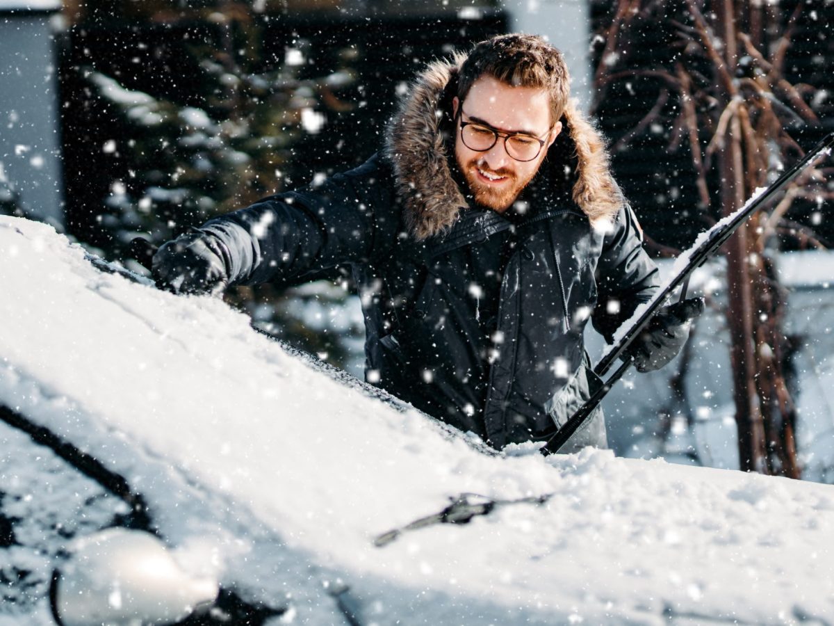 Mann befreit sein Auto von Schnee und Eis.