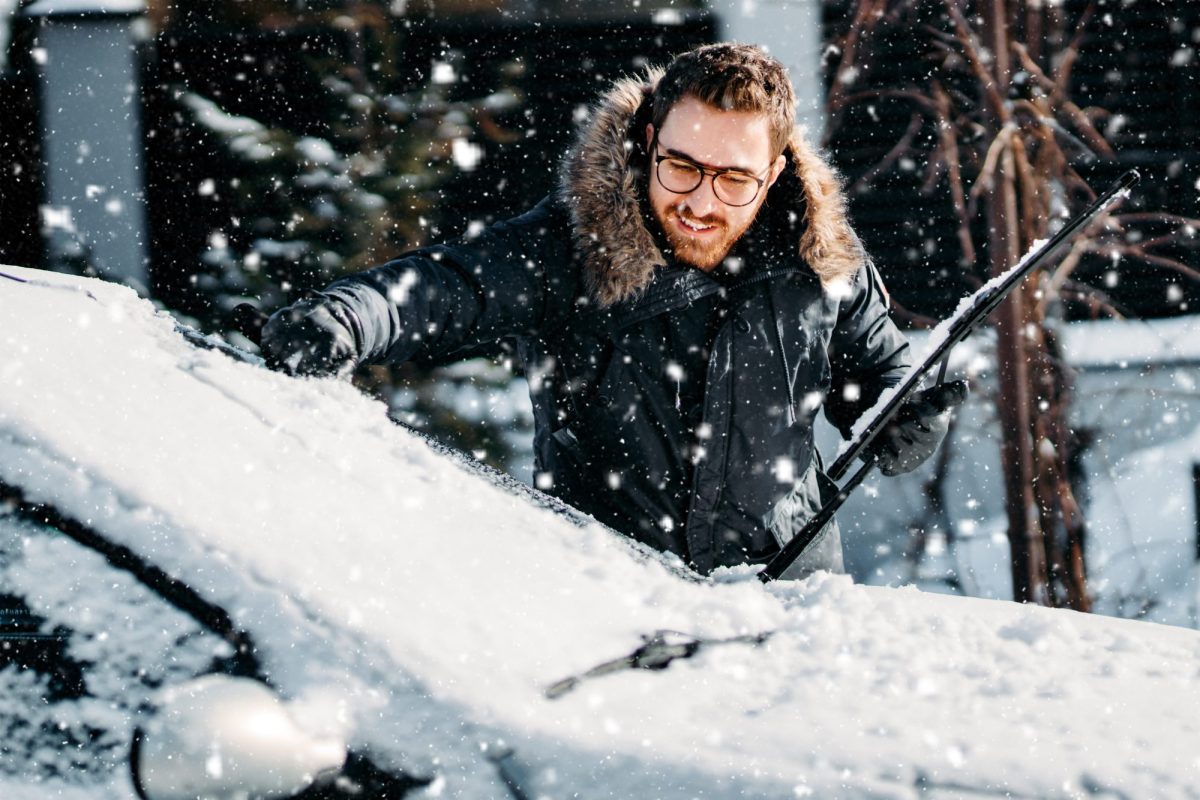 Mann befreit sein Auto von Schnee und Eis.