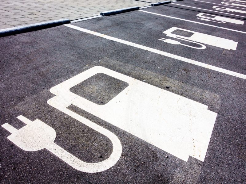 Symbol einer LadesÃ¤ule fÃ¼r Elektroautos ist auf den StraÃŸenbelag gezeichnet.