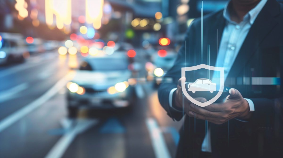 Man hÃ¤lt ein Smartphone in der Hand, darÃ¼ber sieht man ein holografisches Emblem mit einem Auto umrahmt von einem Schutzschild.