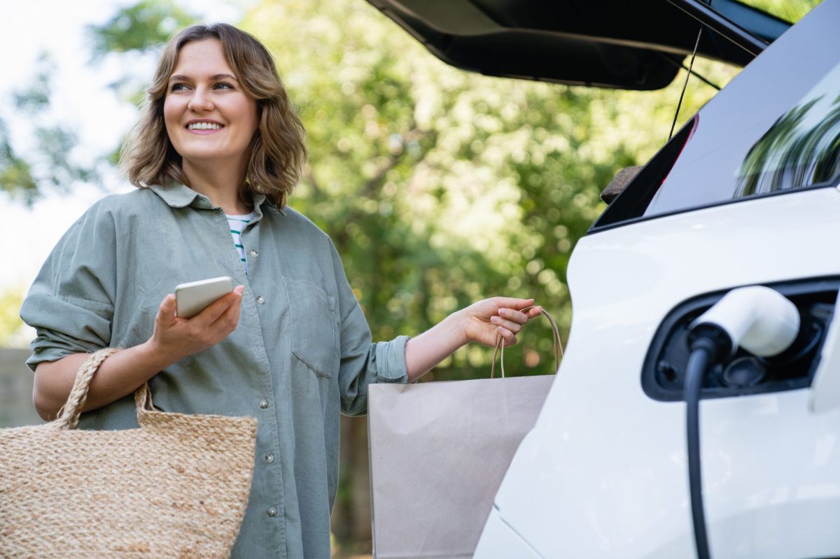 Frau lÃ¤dt EinkÃ¤ufe in den Kofferraum, wÃ¤hrend ihr Elektroauto geladen wird.