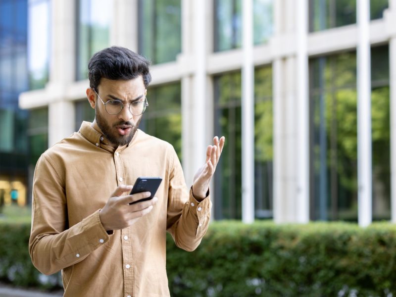 Mann blickt genervt auf sein Handy.
