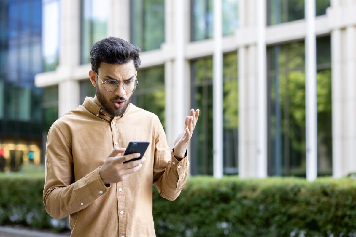 Mann blickt genervt auf sein Handy.