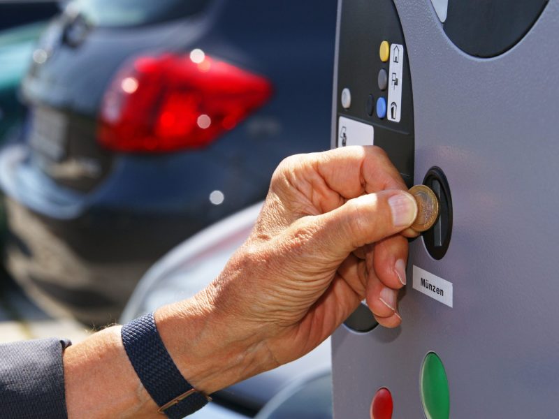 Eine Person wirft eine Münze in eine Parkscheinautomaten.