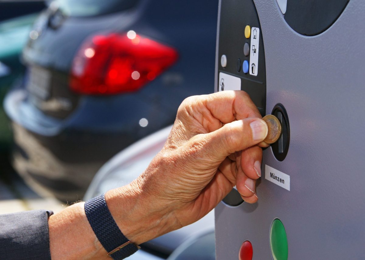 Eine Person wirft eine MÃ¼nze in eine Parkscheinautomaten.