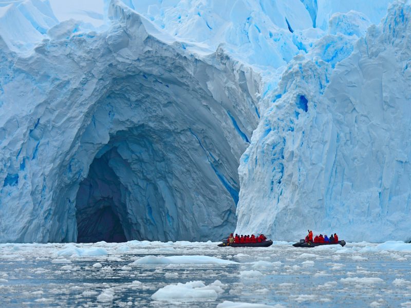 Zwei Boote mit zahlreichen Passagieren stehen vor der Öffnung einer riesigen Höhle in einem Gletscher.