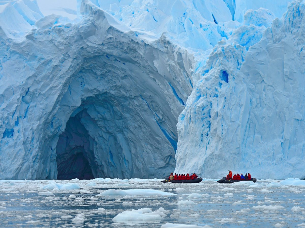 Zwei Boote mit zahlreichen Passagieren stehen vor der Öffnung einer riesigen Höhle in einem Gletscher.