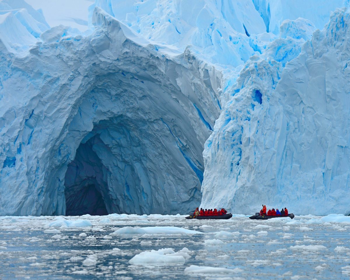 Zwei Boote mit zahlreichen Passagieren stehen vor der Öffnung einer riesigen Höhle in einem Gletscher.